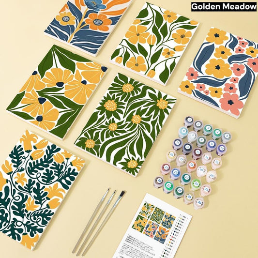a collection of six patterned notebooks, paintbrushes, and paint tubes arranged on a light-colored surface.