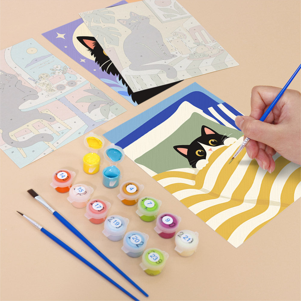 a person's hand holding a paintbrush, surrounded by art supplies such as paint tubes and brushes, as well as a partially completed painting featuring a cat.