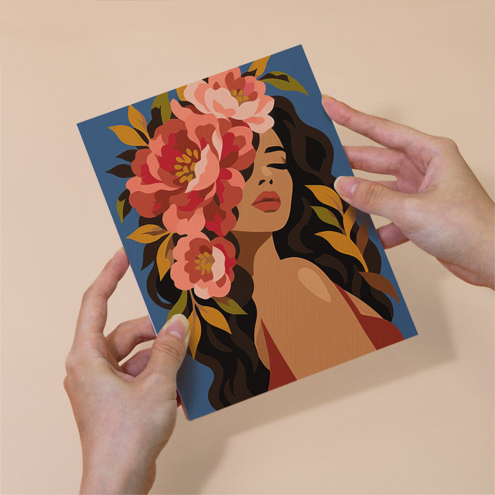 A person's hands are holding a card with a colorful illustration of a woman's face surrounded by flowers.
