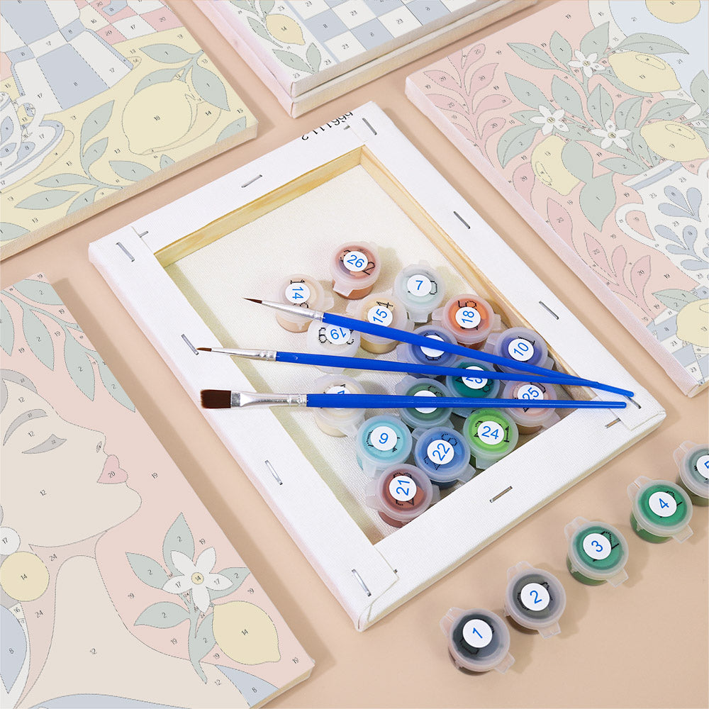 a painting kit with a canvas, paintbrushes, and multiple paint color bottles arranged on a table.