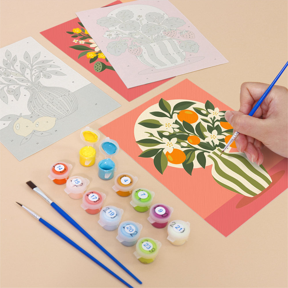 a person's hand painting a floral design on a piece of paper using a paintbrush, surrounded by various art supplies such as paint tubes and brushes.