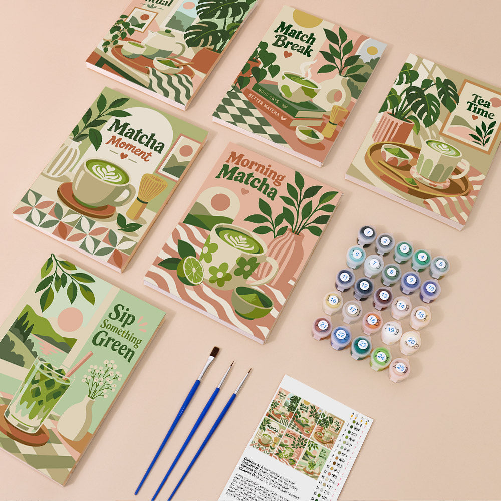 various art supplies, including paintbrushes, paint tubes, and a book with illustrations of green tea and plants.