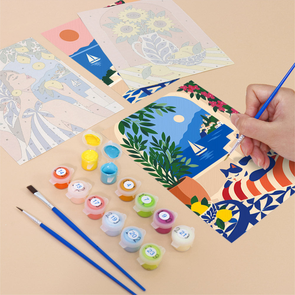 a hand holding a paintbrush, surrounded by art supplies such as paint tubes and brushes, as well as a partially completed painting depicting a beach scene with a boat and palm trees.