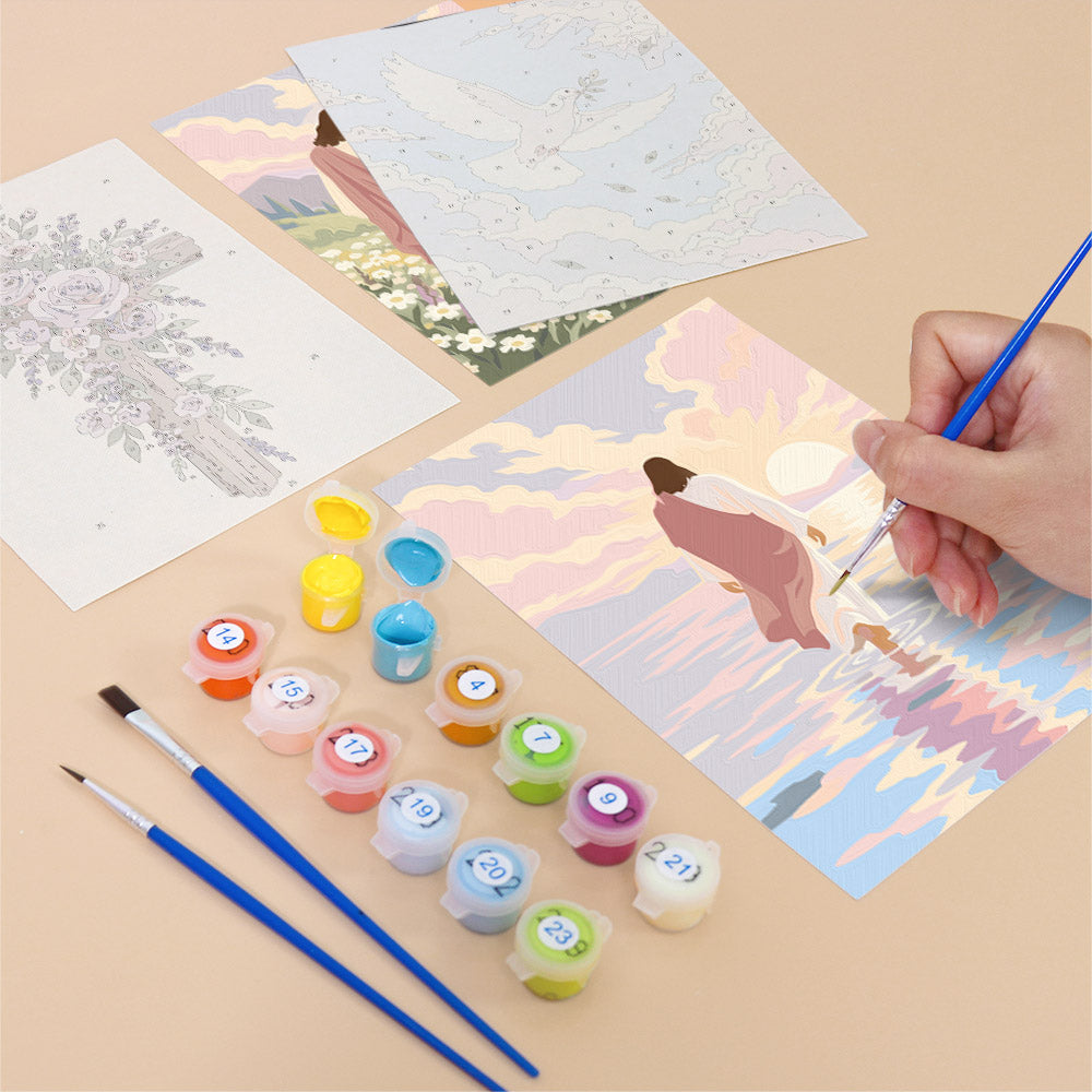a person's hand holding a paintbrush, surrounded by art supplies such as paint tubes and brushes, as well as a painting depicting a serene landscape with a figure in a pink dress.