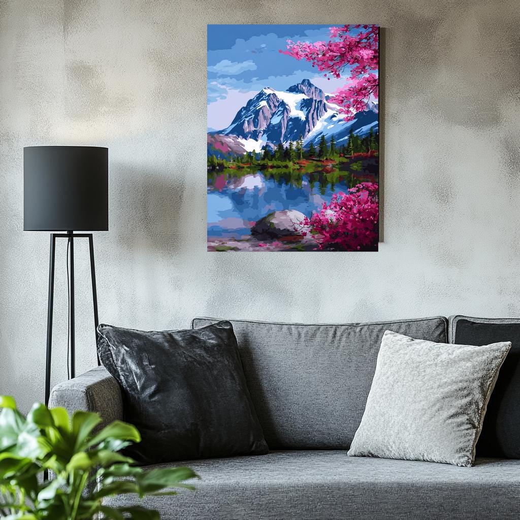 a cozy living room with a gray couch, a black floor lamp, and a framed painting of a mountain landscape with a lake and pink flowers hanging on the wall.