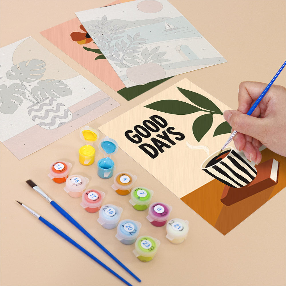 a hand holding a paintbrush, surrounded by various art supplies such as paint tubes, brushes, and a "Good Days" card.
