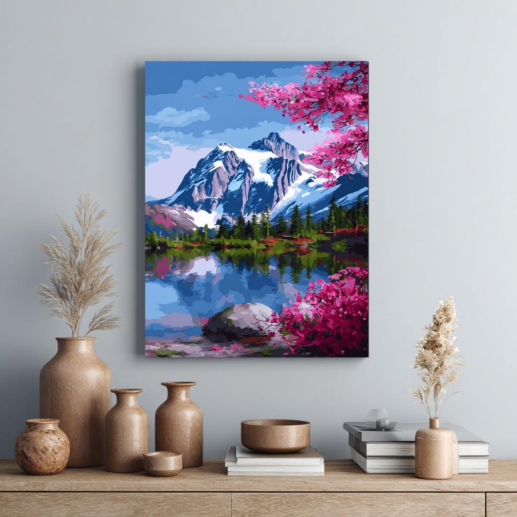 a painting of a mountain landscape with a lake and pink flowers, hanging on a wall above a wooden shelf with various decorative items such as vases and books.
