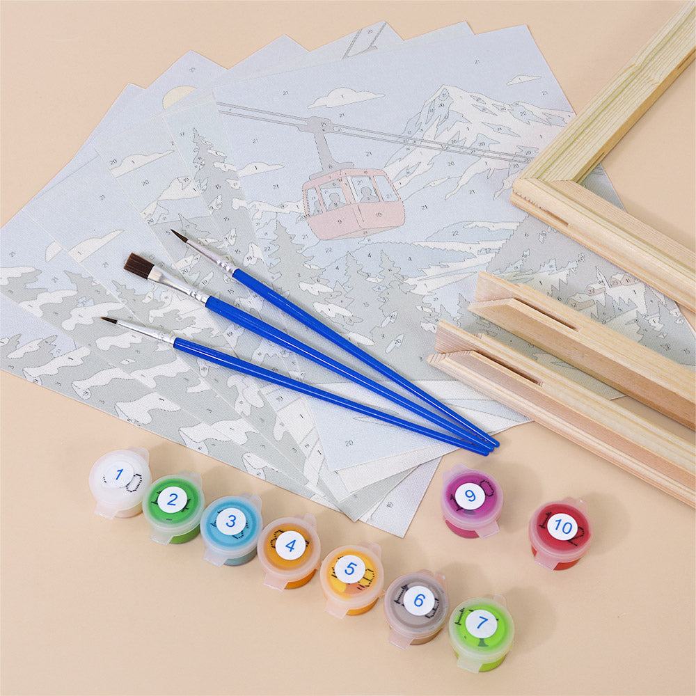 various art supplies, including paintbrushes, paint tubes, and a coloring book with a mountain scene and a ski lift illustration.