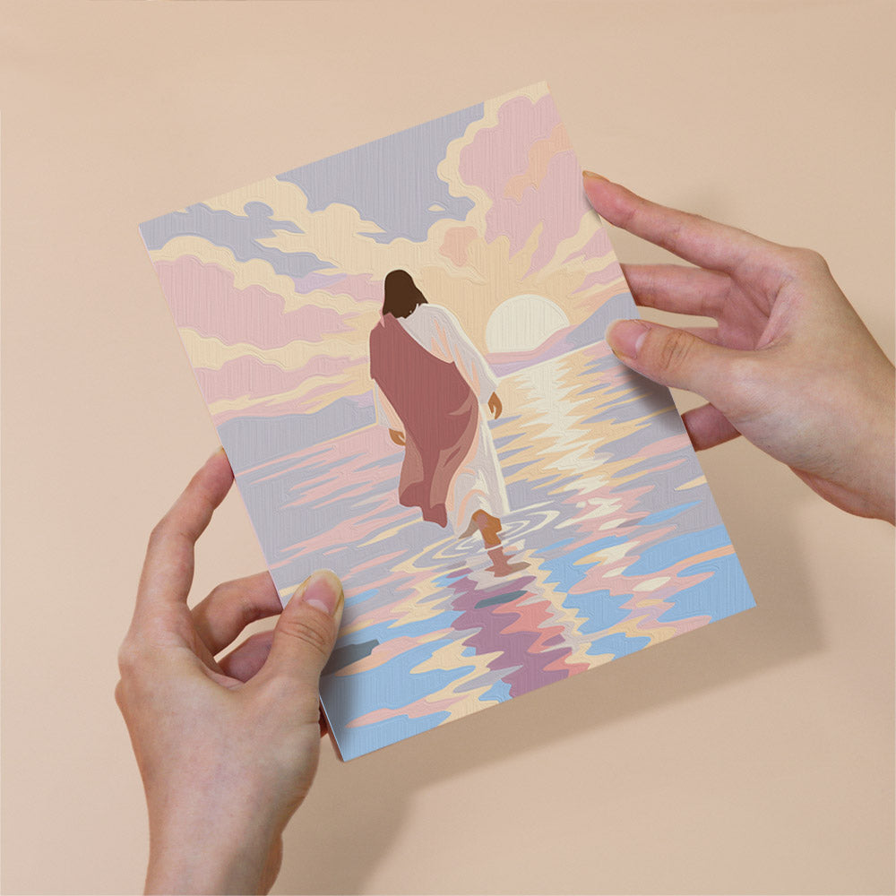 A person's hands are holding a piece of paper with an illustration of a person walking in water, with a sunset in the background.