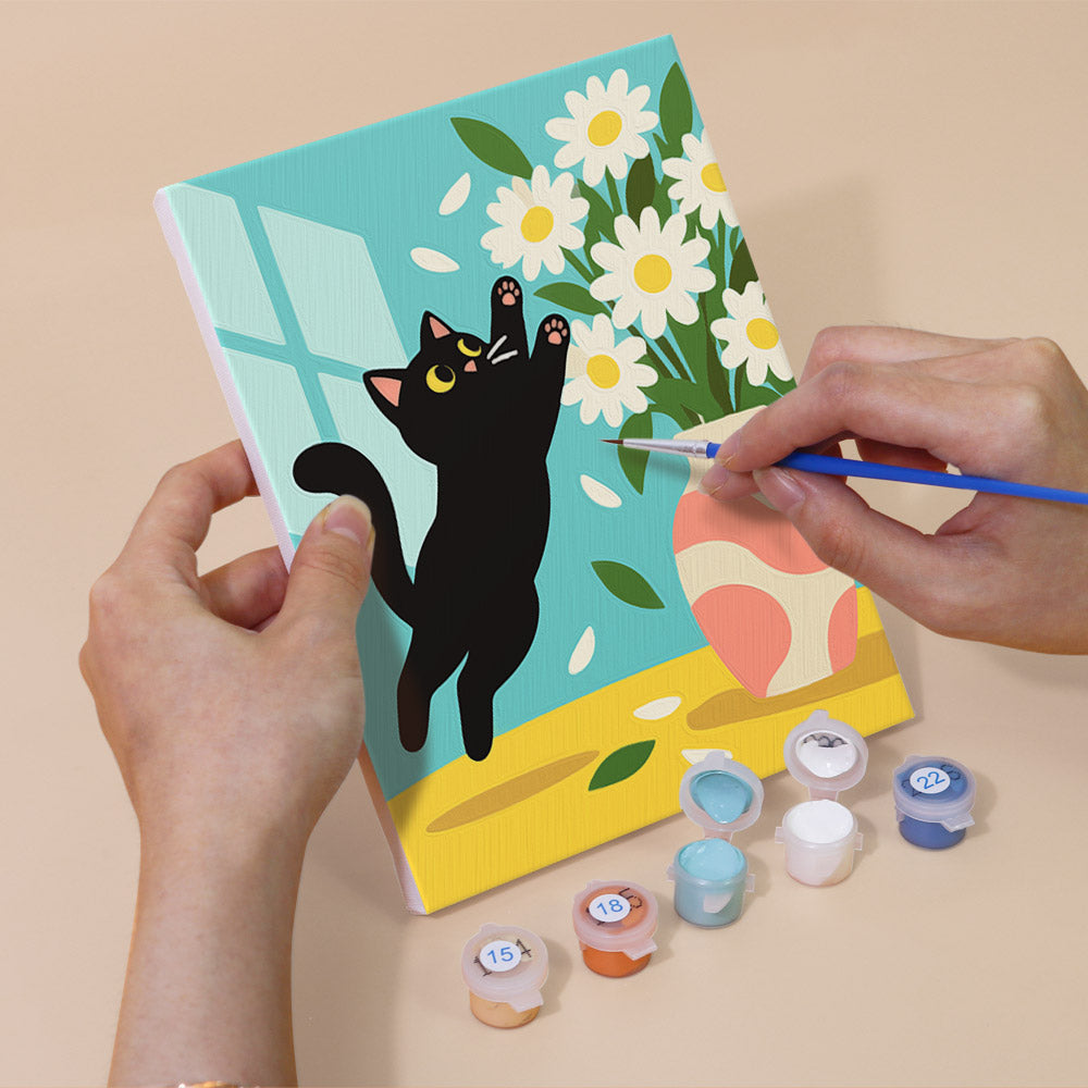 A person's hands are holding a canvas with a black cat and a vase of flowers, and there are paint bottles and a paintbrush nearby, suggesting that the image is a painting kit.