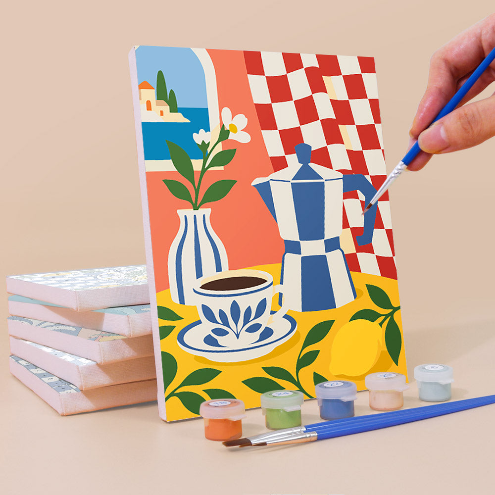 A hand is painting a colorful canvas depicting a still life scene with a vase, coffee cup, and lemon, along with a checkered tablecloth and a stack of books.