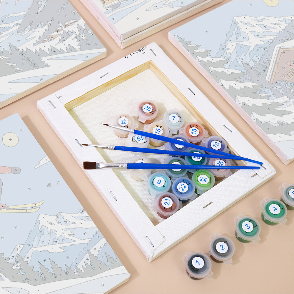 a painting kit with a canvas, paintbrushes, and multiple paint color bottles arranged on a table.