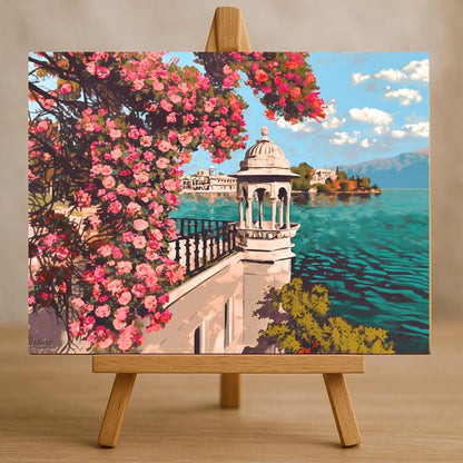 The image is a painting of a picturesque scene featuring a white building with a dome, surrounded by a lush garden with pink flowers, overlooking a serene body of water.