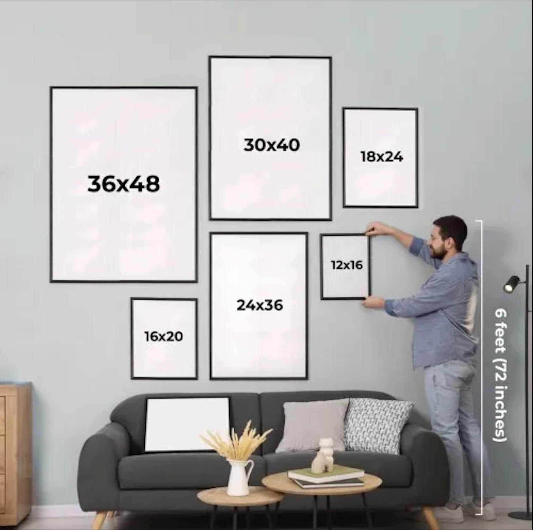 A man is hanging a series of framed artworks on a wall in a living room.