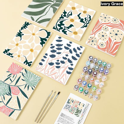 a collection of art supplies, including paintbrushes, paint tubes, and patterned papers, arranged on a light-colored surface.
