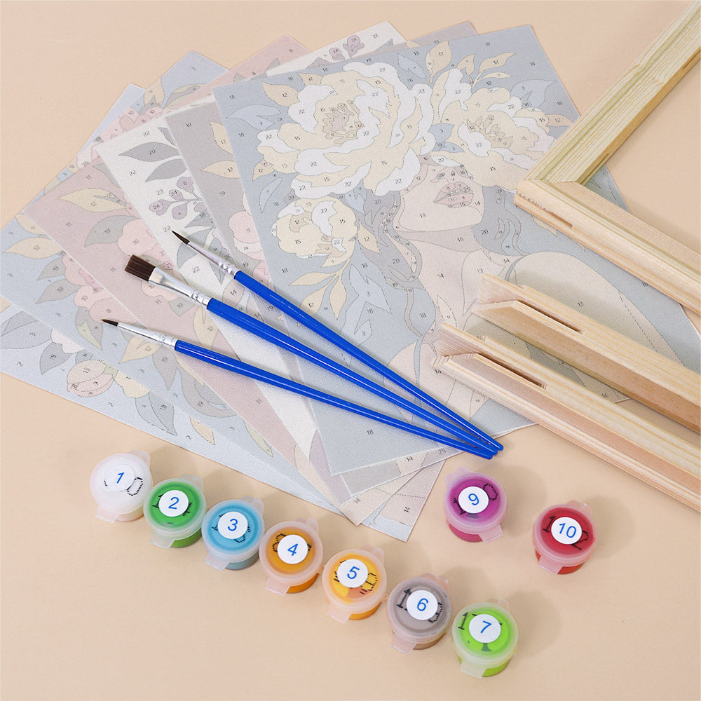 various art supplies, including paintbrushes, paint tubes, and a floral pattern, arranged on a light-colored surface.