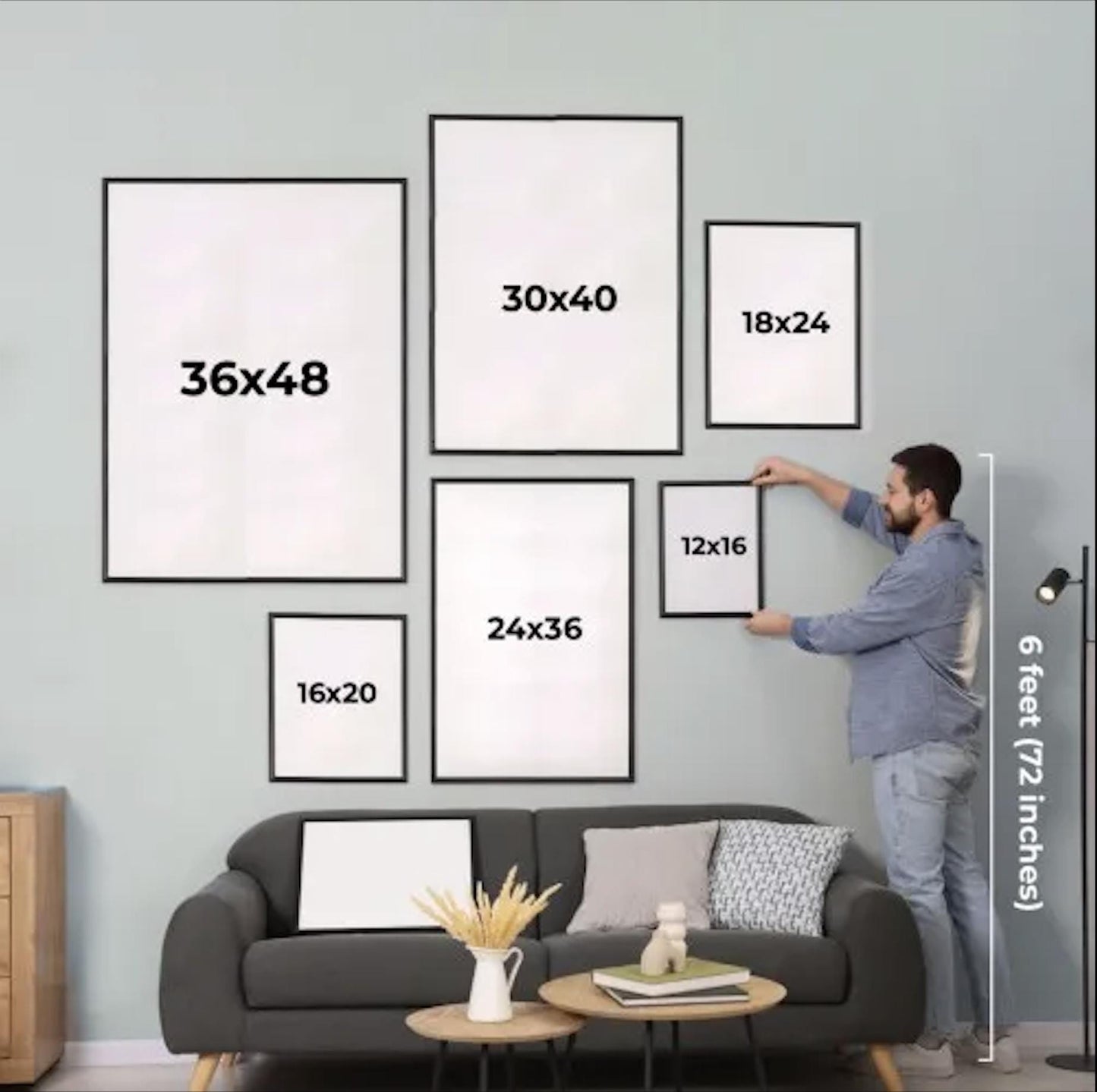 A man is hanging a series of framed artworks on a wall in a living room.