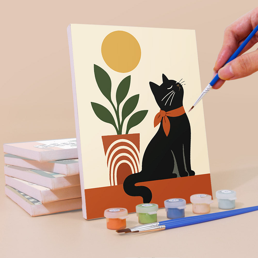 A hand is painting a picture of a black cat sitting on a windowsill, with a potted plant and a stack of books nearby.
