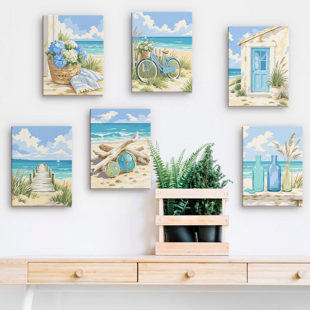 a wall with six framed paintings depicting various beach scenes, including a bicycle, a basket of flowers, a house, a beach path, and a plant.